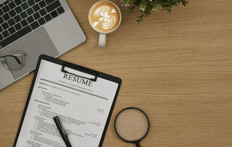 A resume on a clipboard, a laptop, a laptop, glasses, cup of coffee, a plant on a wooden desk